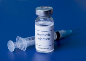 Antibiotic injection vial with syringe on blue background.