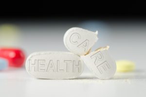 Stack of pills with HEALTH CARE stamped into them, the CARE pills is broken in half representing a broken Health Care system and medical care.